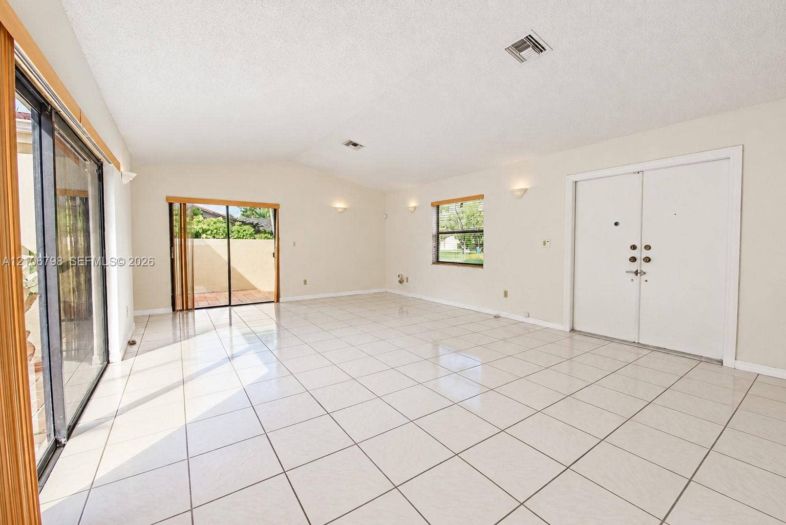 14750 SW 156th Street, Miami, FL 33187 Interior space featuring large-format tile flooring, high vaulted ceilings, double-entry doors, dual sliding glass door systems, and wall-mounted sconce lighting