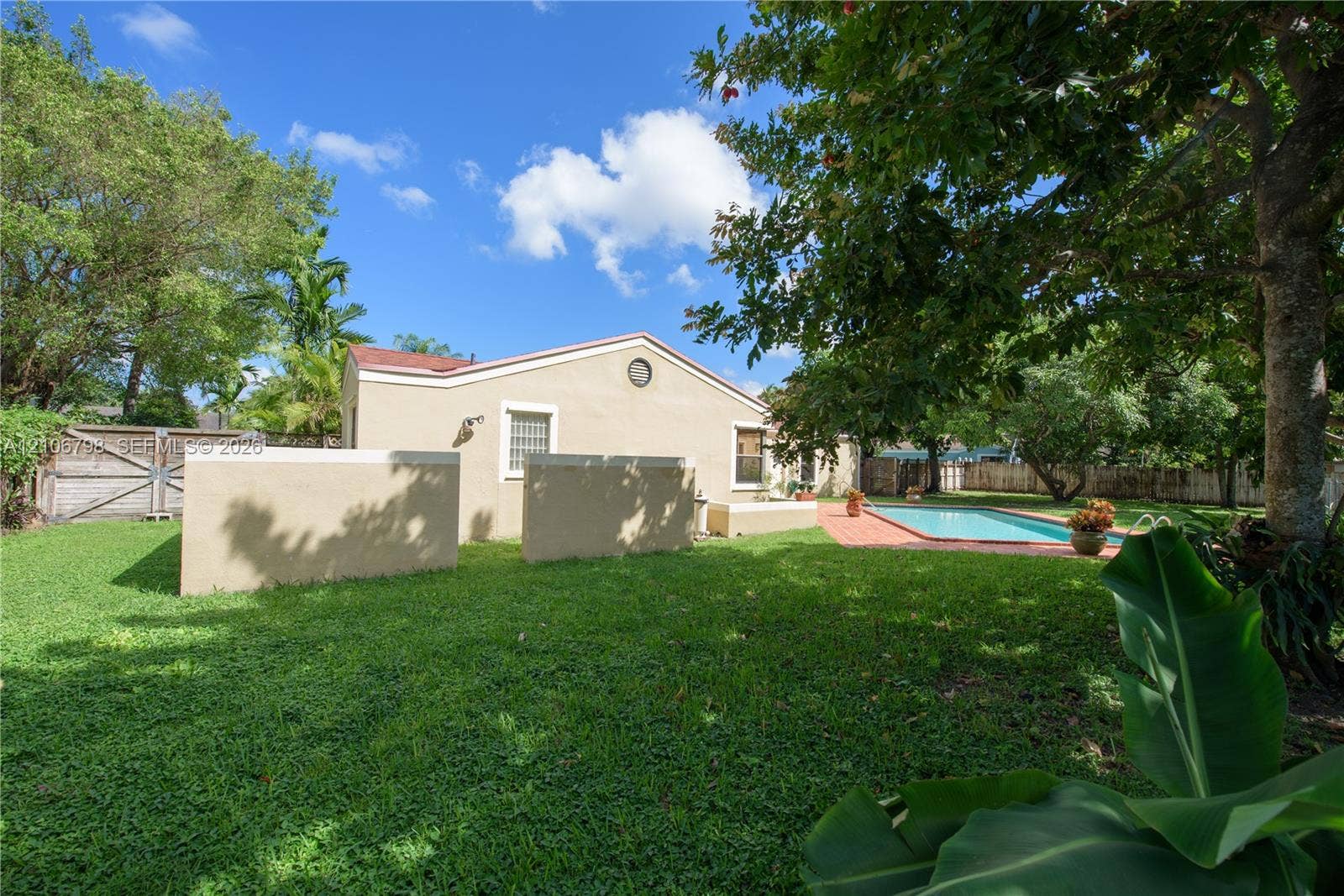 14750 SW 156th Street, Miami, FL 33187 Expansive backyard featuring a manicured lawn, inground swimming pool, paved patio, perimeter wood fencing, and mature trees