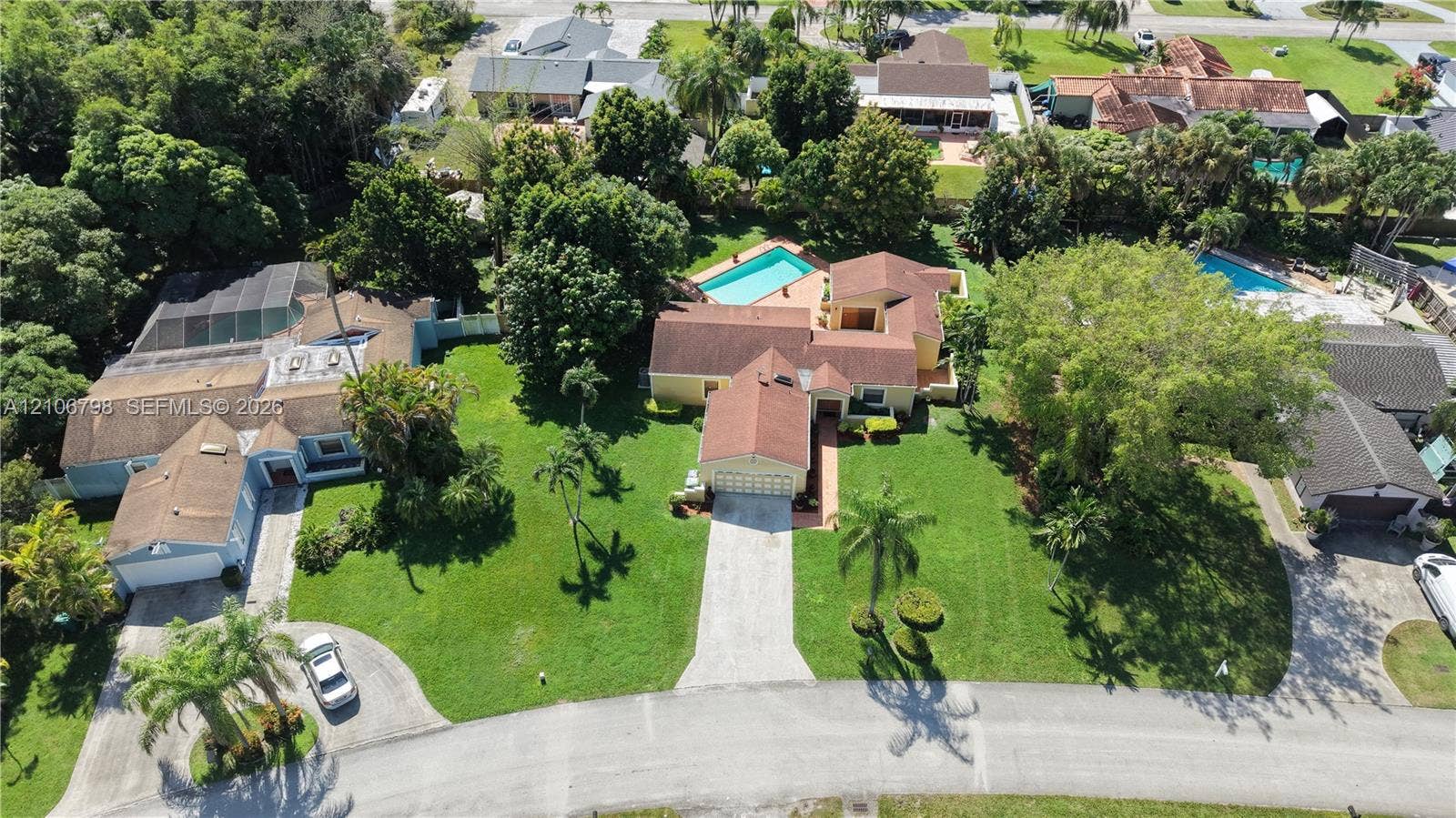 14750 SW 156th Street, Miami, FL 33187 Aerial perspective of a sprawling corner lot featuring a multi-gable roofline, an attached multi-car garage, paved driveway, and an in-ground swimming pool