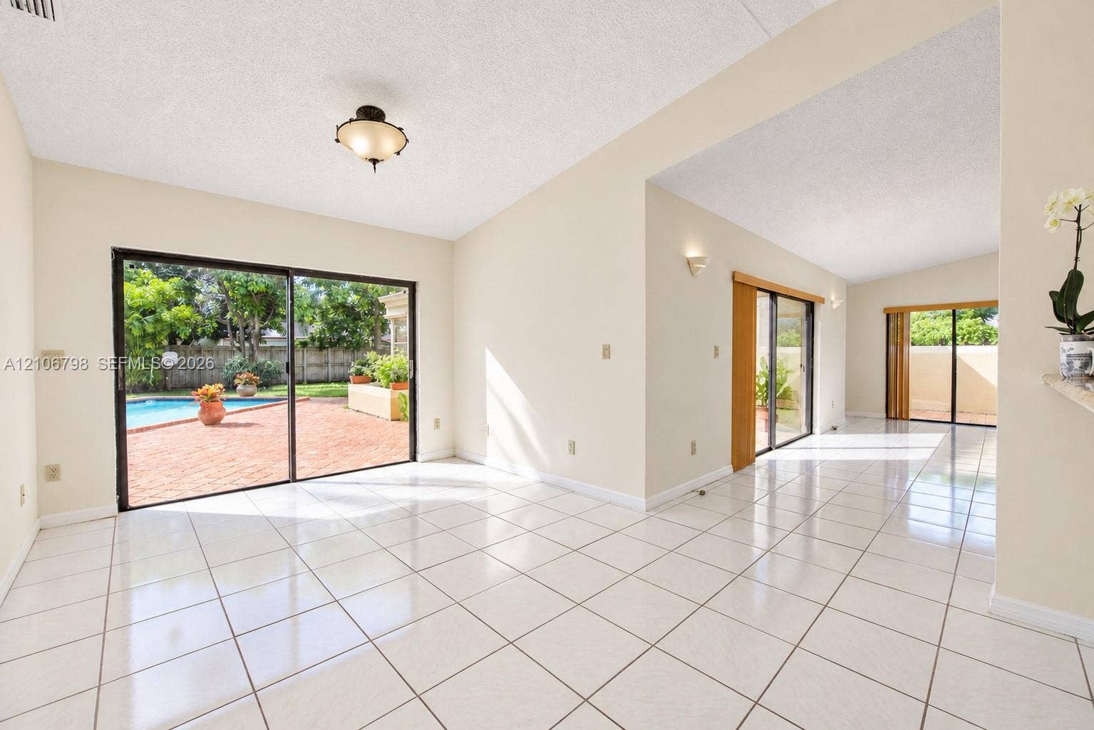 14750 SW 156th Street, Miami, FL 33187 Interior space featuring light-colored tile flooring, vaulted ceilings, multiple sliding glass doors, flush-mount and wall-mounted lighting, and a private outdoor area with a swimming pool