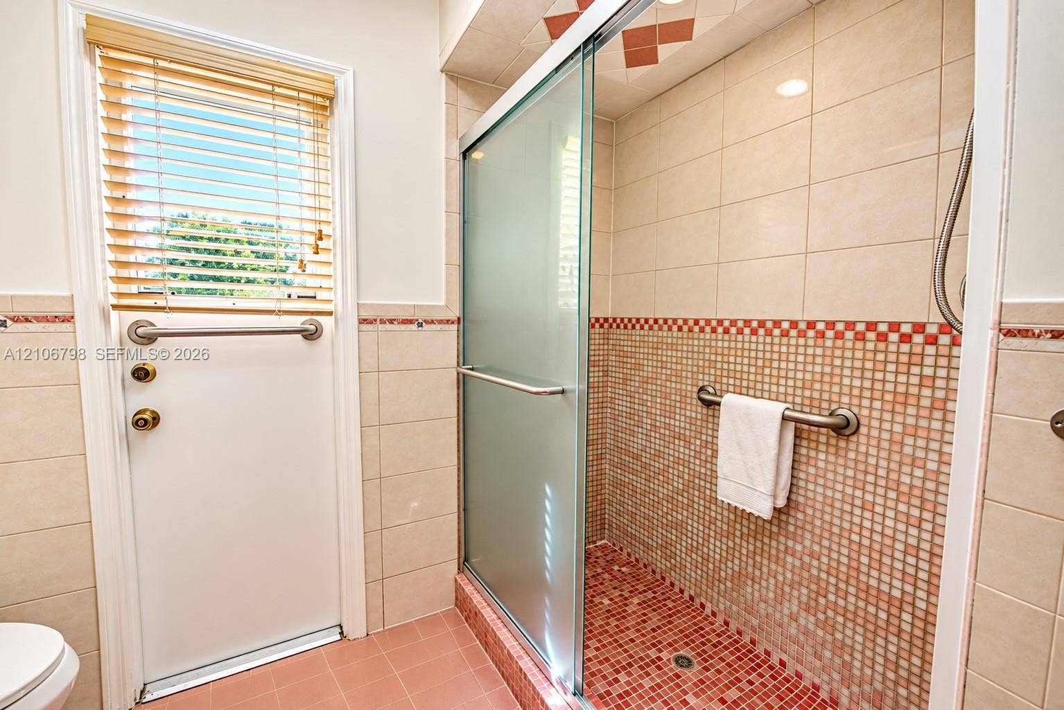 14750 SW 156th Street, Miami, FL 33187 Walk-in shower featuring a glass sliding door, mosaic tile detailing, wall-mounted safety grab bars, and neutral wall tile