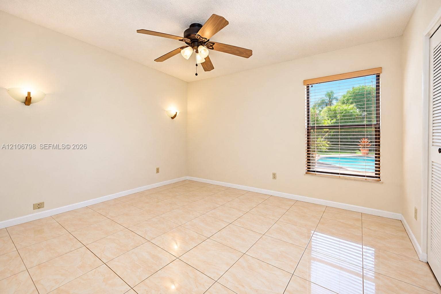 14750 SW 156th Street, Miami, FL 33187 Neutral-toned tile flooring, ceiling fan with integrated light fixture, dual wall-mounted light sconces, louvered closet doors, and window with built-in blinds