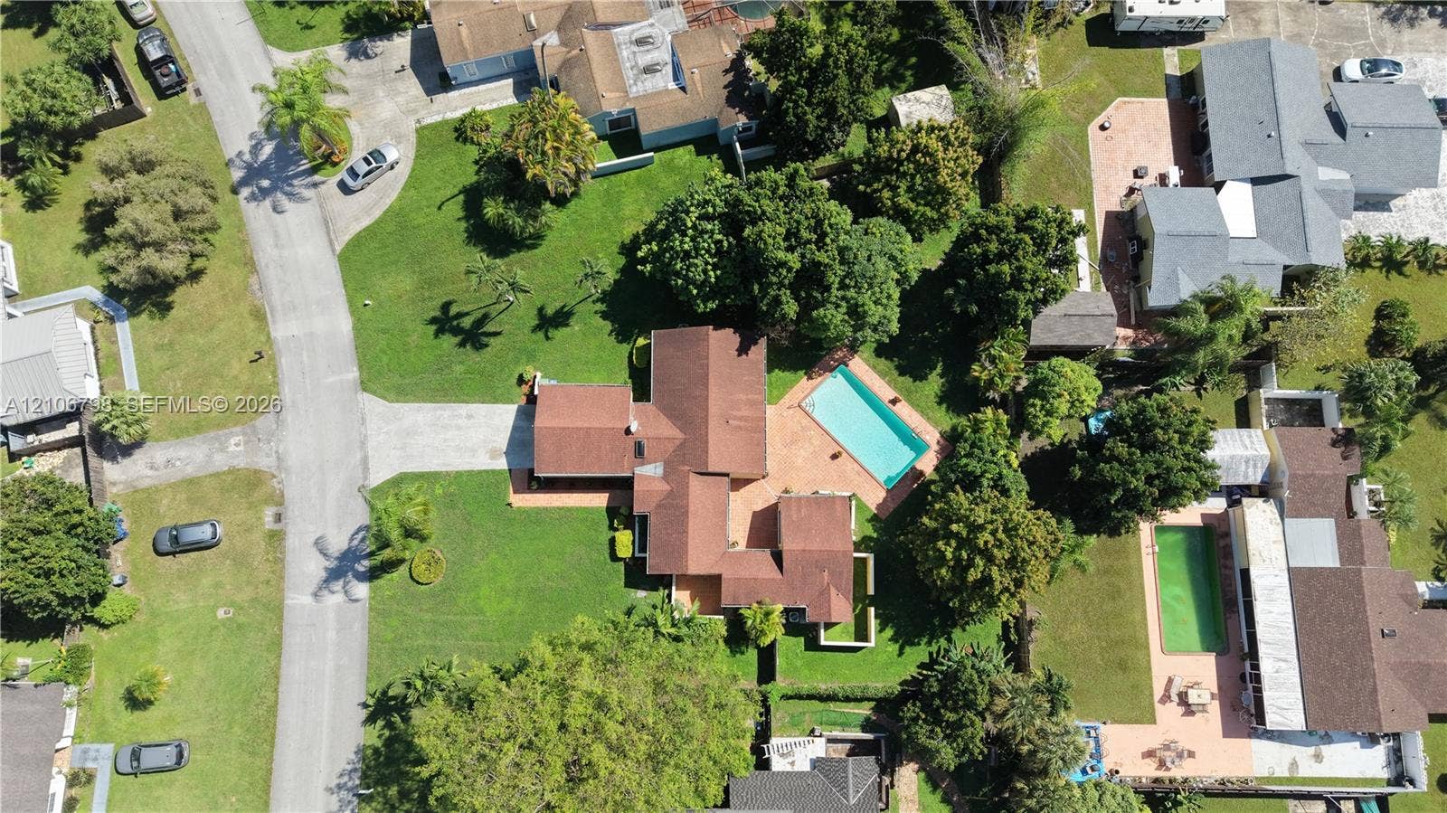14750 SW 156th Street, Miami, FL 33187 Aerial perspective of a property featuring a multi-gabled shingle roof, paved driveway, expansive lawn, mature landscaping, and an inground swimming pool with a paved patio