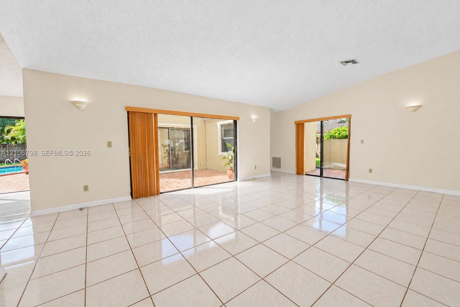 14750 SW 156th Street, Miami, FL 33187 Spacious interior featuring vaulted ceilings, oversized ceramic tile flooring, dual sliding glass door systems, and wall-mounted sconce lighting