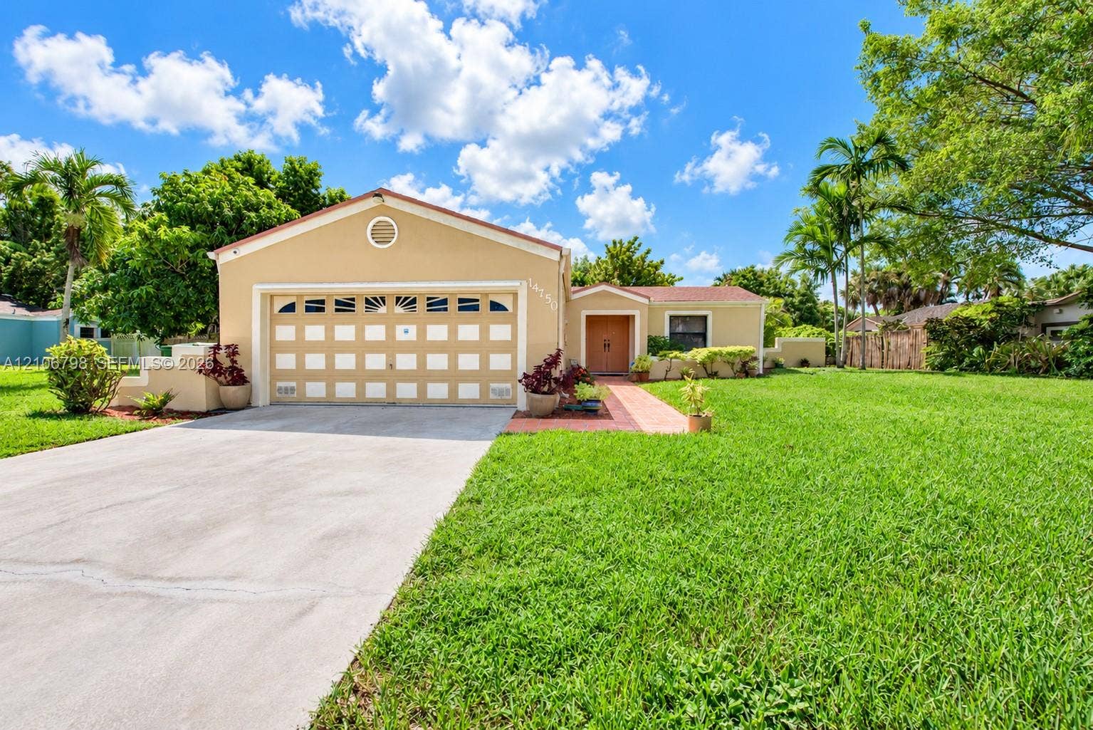 14750 SW 156th Street, Miami, FL 33187 Stucco exterior featuring a two-car garage with arched decorative windows, concrete driveway, tiled entryway path, and expansive manicured lawn