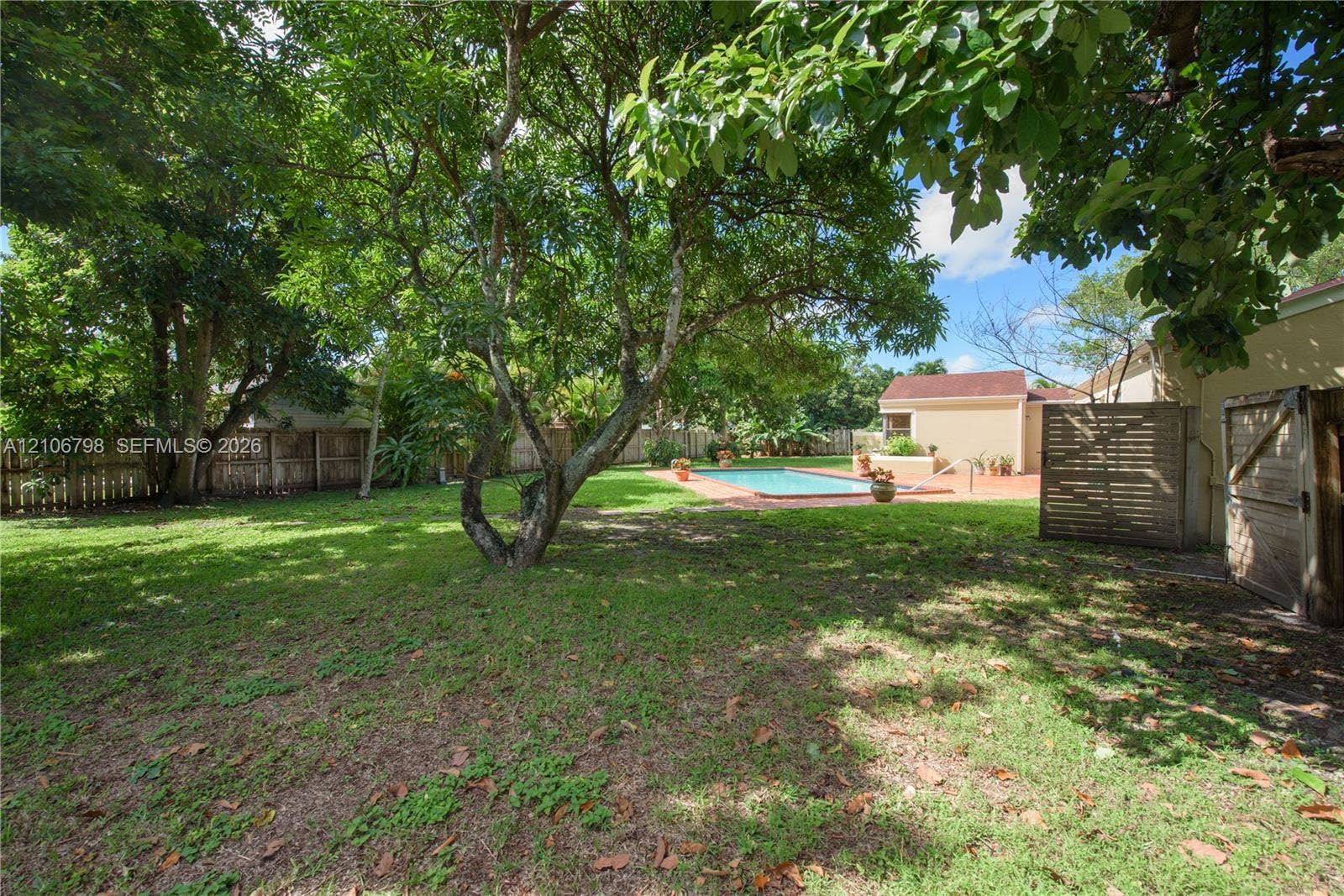 14750 SW 156th Street, Miami, FL 33187 Expansive backyard featuring mature shade trees, a perimeter wood fence, in-ground swimming pool, and a brick-paver patio area