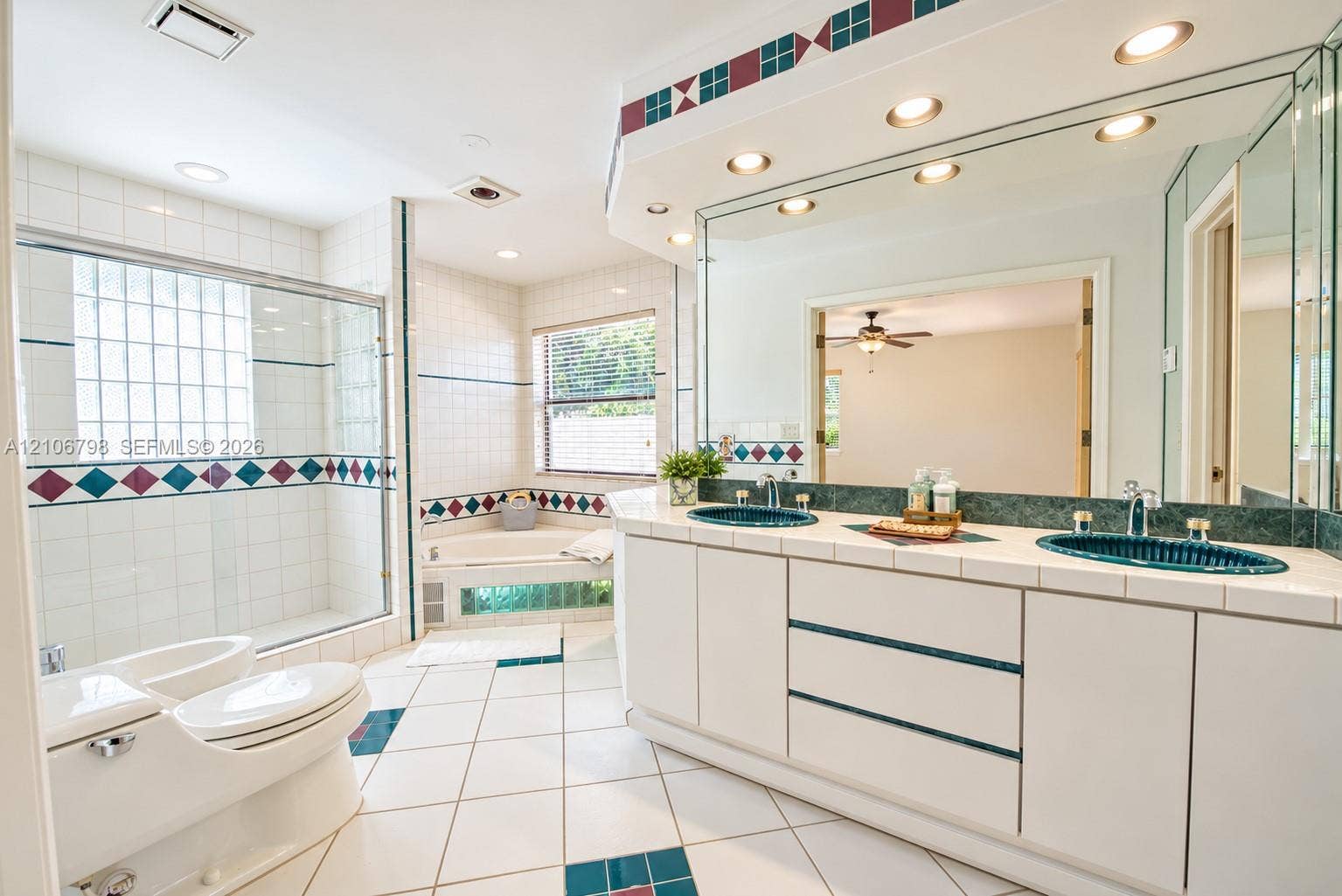 14750 SW 156th Street, Miami, FL 33187 Dual-vanity cabinet featuring white cabinetry, tile countertop, and inset glass sinks with a large wall-to-wall mirror