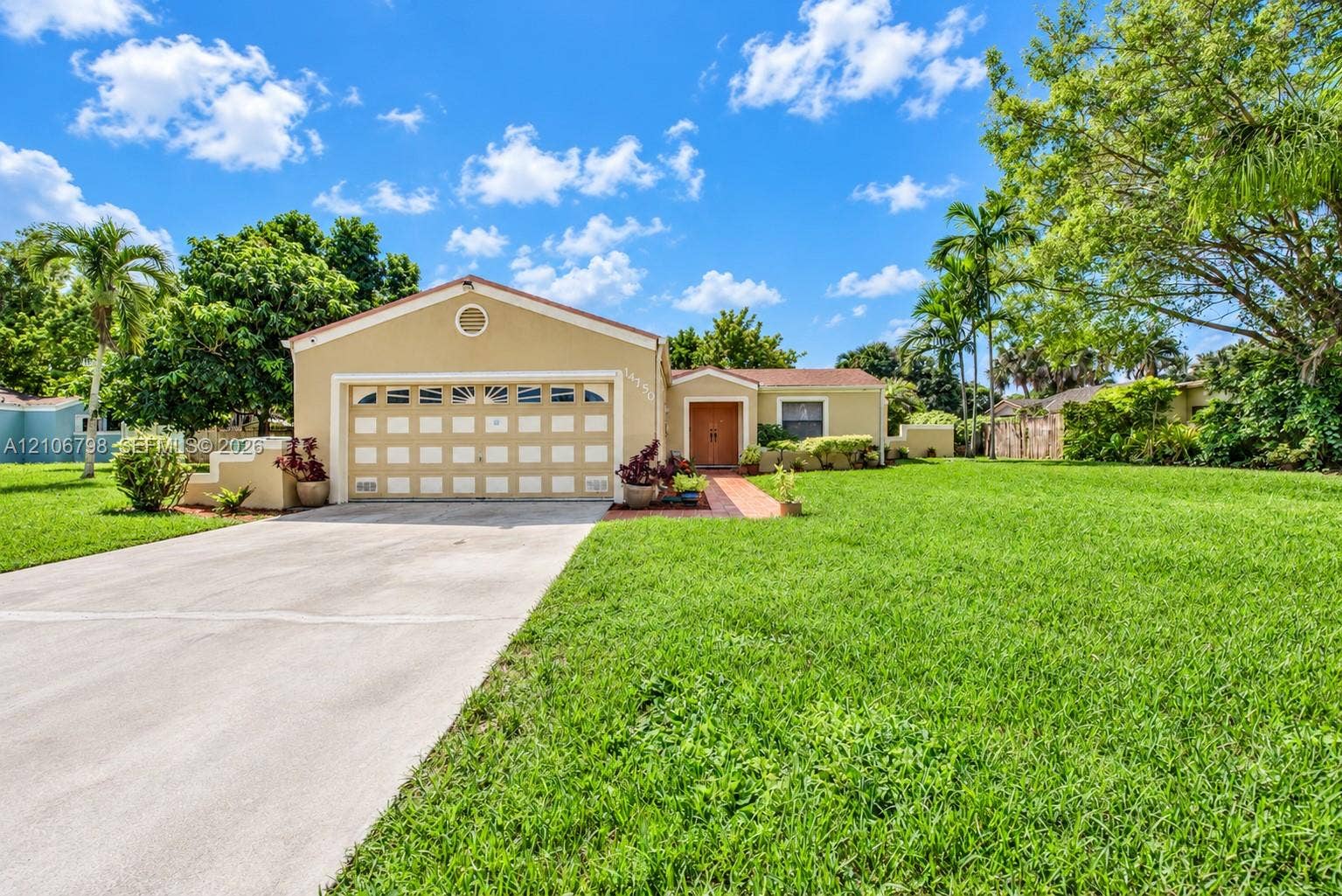 14750 SW 156th Street, Miami, FL 33187 Single-story residence featuring a stucco exterior, multi-pane garage door, concrete driveway, and a paved walkway leading to the entrance, set on a property with mature landscaping