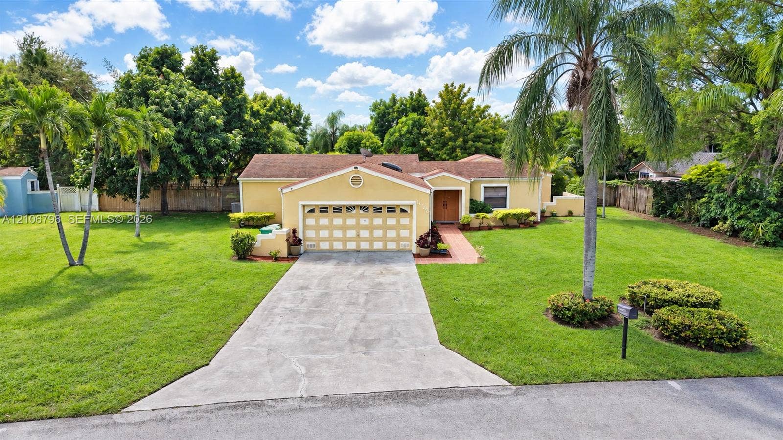 14750 SW 156th Street, Miami, FL 33187 Single-story residence featuring a multi-car garage, concrete driveway, tiled roof, and extensive lawn landscaping with mature palm trees