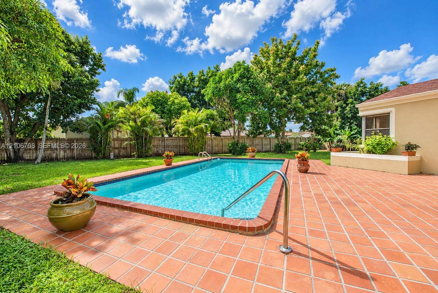14750 SW 156th Street, Miami, FL 33187 Rectangular swimming pool featuring a brick-tiled deck, metal handrail, and integrated raised masonry seating wall