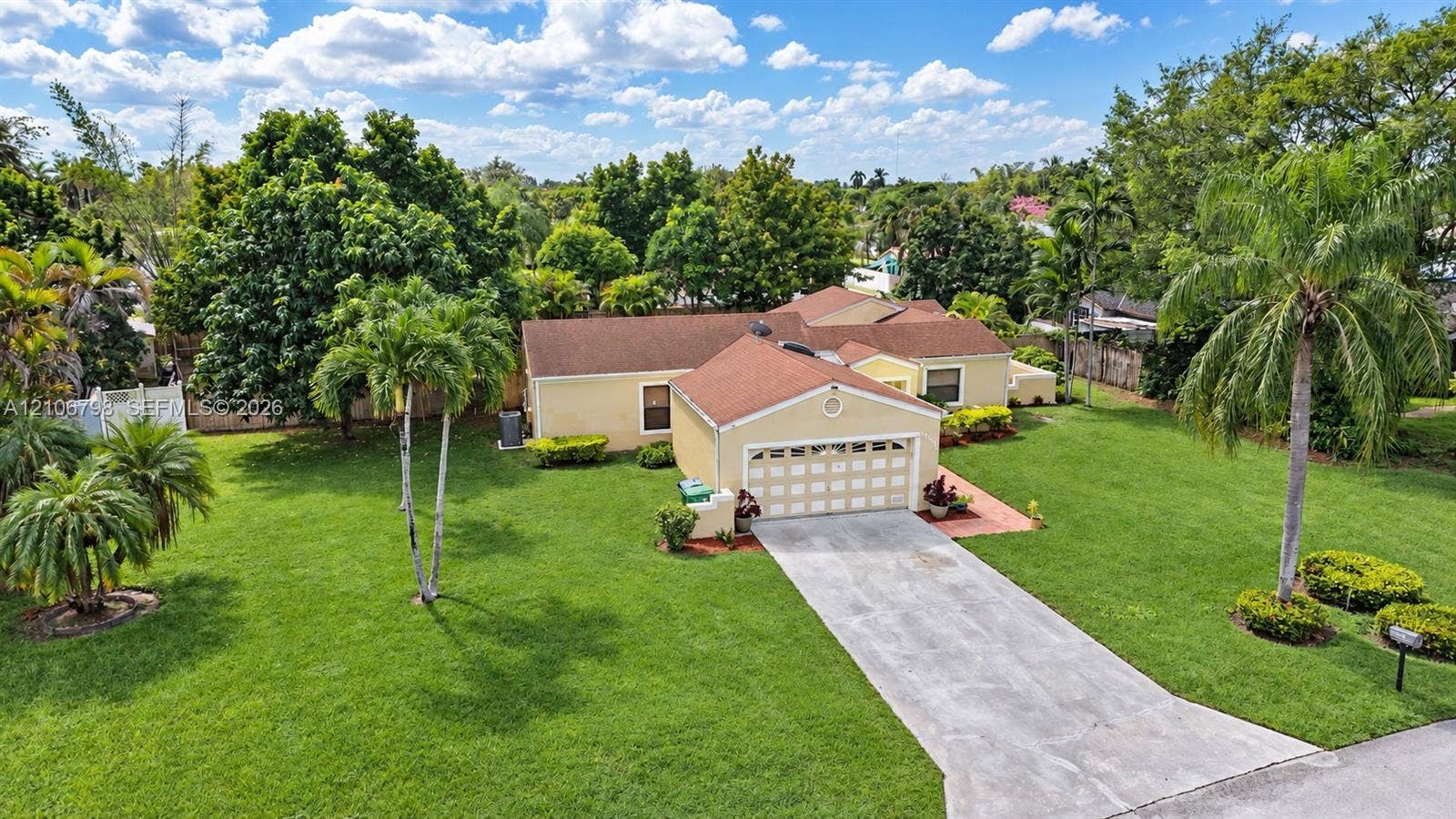 14750 SW 156th Street, Miami, FL 33187 Single-story residence featuring a multi-gabled shingle roof, two-car garage, concrete driveway, and expansive lawn with mature landscaping