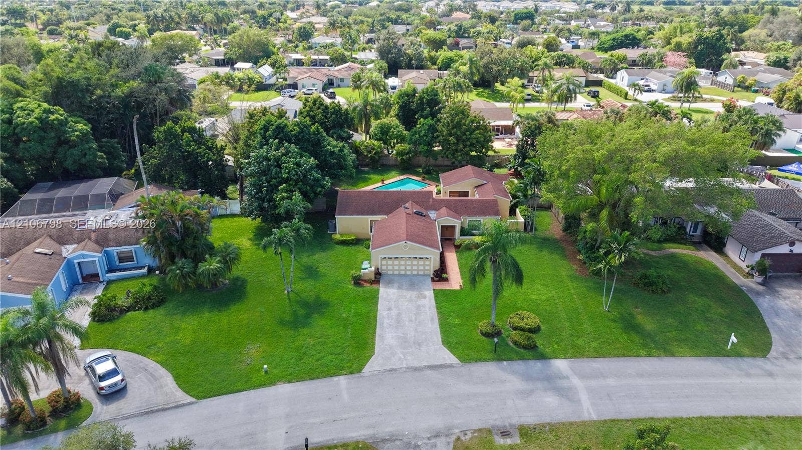14750 SW 156th Street, Miami, FL 33187 Aerial perspective featuring a multi-gabled roofline, concrete driveway, attached garage, in-ground swimming pool, and manicured lawn