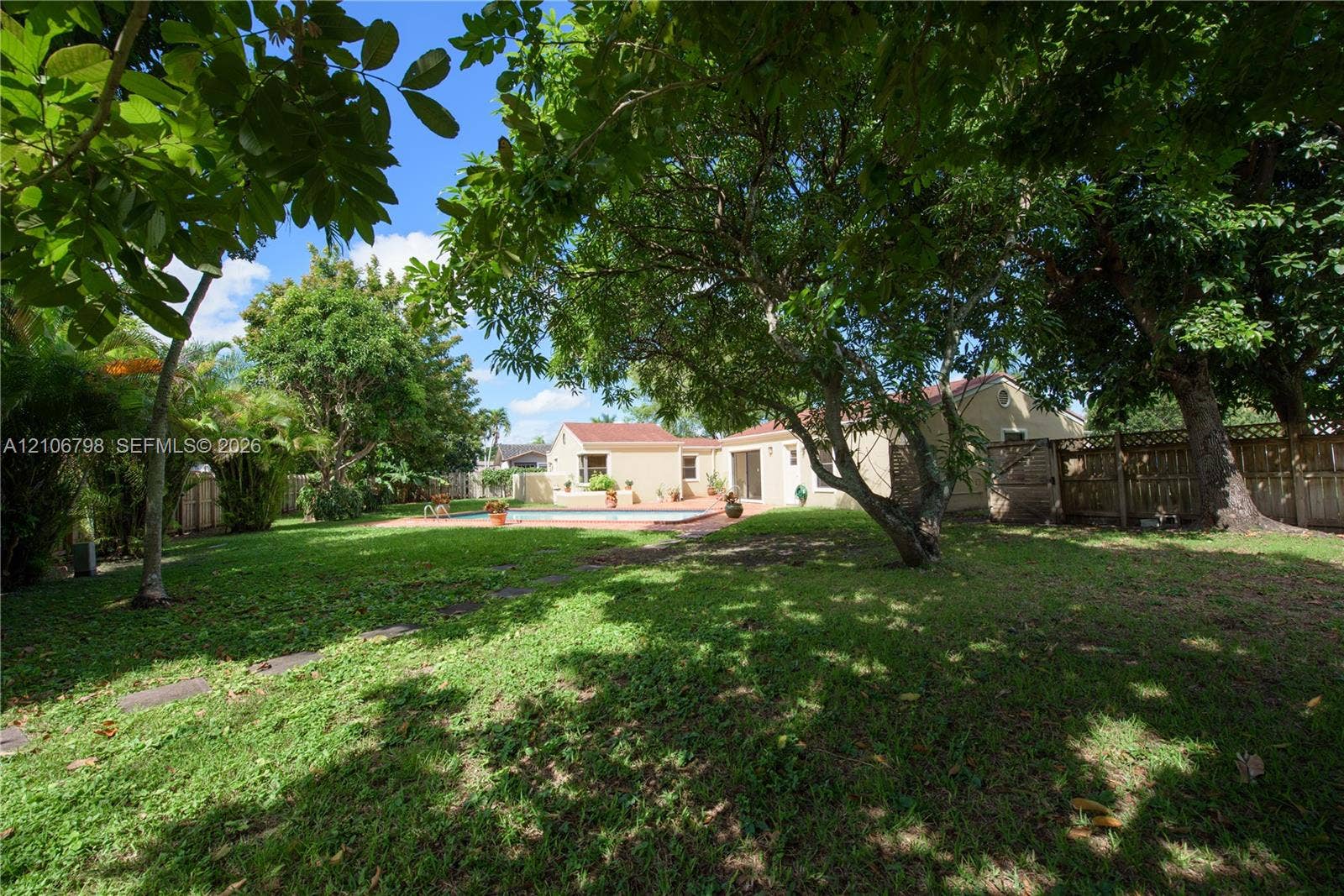 14750 SW 156th Street, Miami, FL 33187 Expansive backyard featuring a large swimming pool, paved patio, mature shade trees, and a wooden perimeter fence