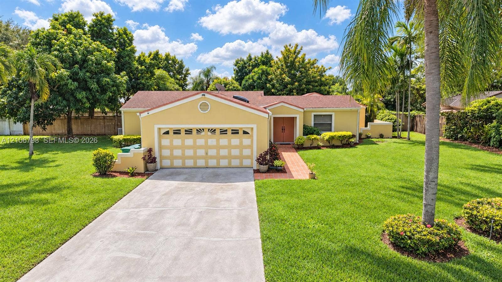14750 SW 156th Street, Miami, FL 33187 Single-story residence featuring a shingled roof, arched garage detailing, brick walkway, and extensive lawn landscaping with mature palms