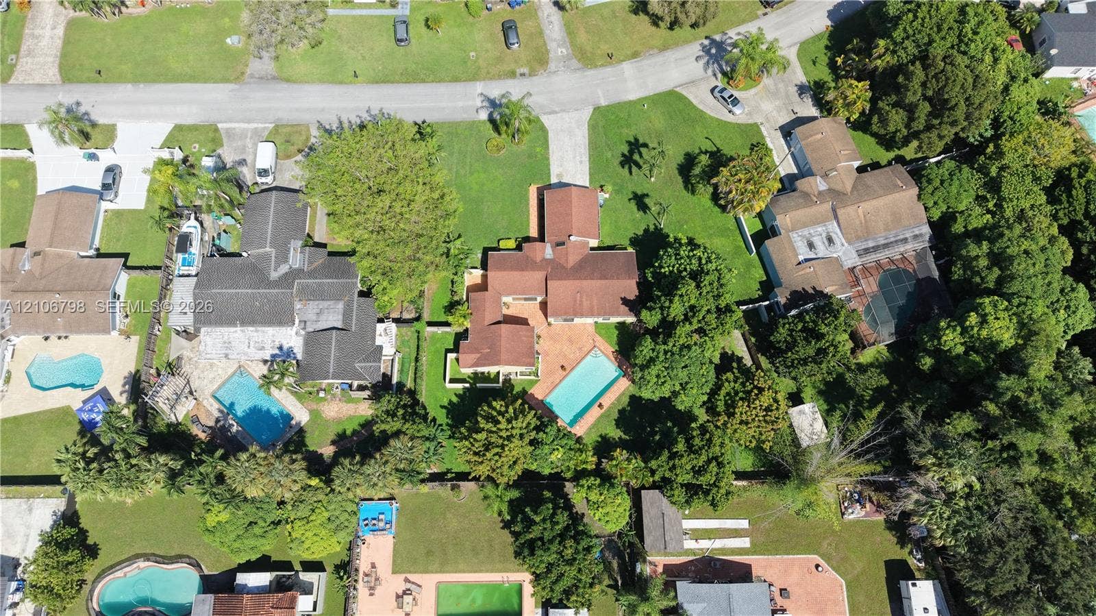 14750 SW 156th Street, Miami, FL 33187 Aerial view featuring a multi-gabled residence with a terracotta-toned shingle roof, a rectangular inground swimming pool, paved patio area, and mature landscaping on a corner lot