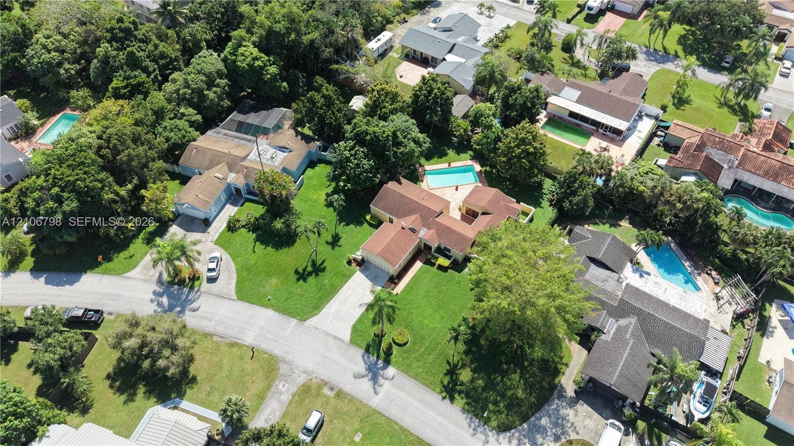 14750 SW 156th Street, Miami, FL 33187 Aerial perspective of a multi-structure property featuring a pitched tile roof, expansive manicured lawn, concrete driveway, and a private swimming pool
