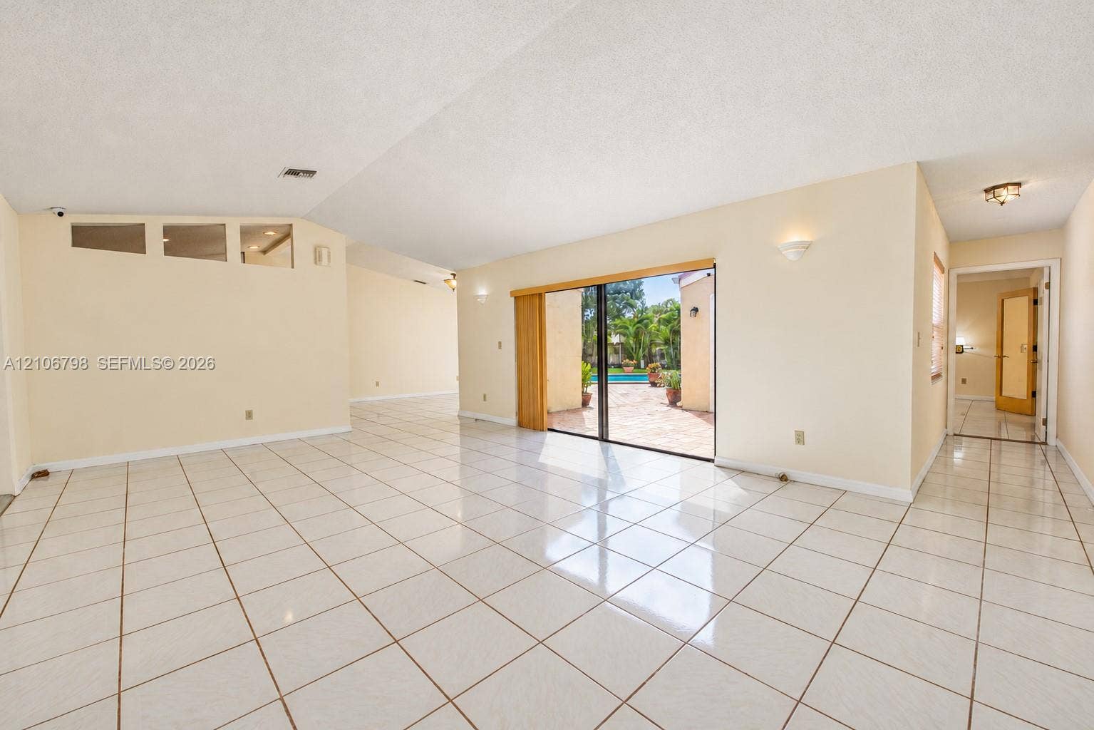 14750 SW 156th Street, Miami, FL 33187 Open-concept interior featuring high ceilings, white tile flooring, recessed wall sconces, clerestory windows, and sliding glass doors