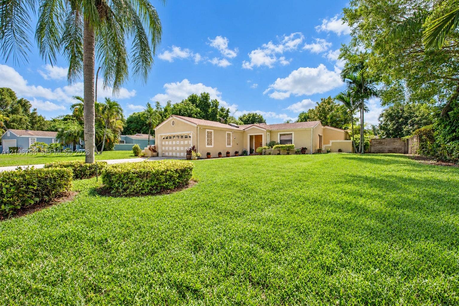 14750 SW 156th Street, Miami, FL 33187 Single-story residence featuring a stucco exterior, multi-car garage, mature tropical landscaping, and an expansive lawn