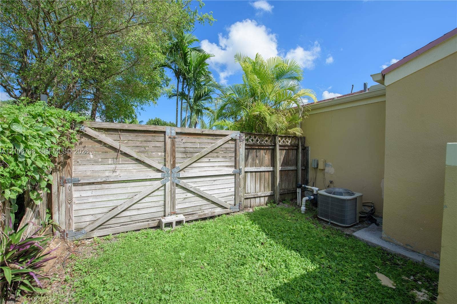 14750 SW 156th Street, Miami, FL 33187 Side yard featuring a wood fence with metal hardware, mature palm trees, and an external HVAC unit