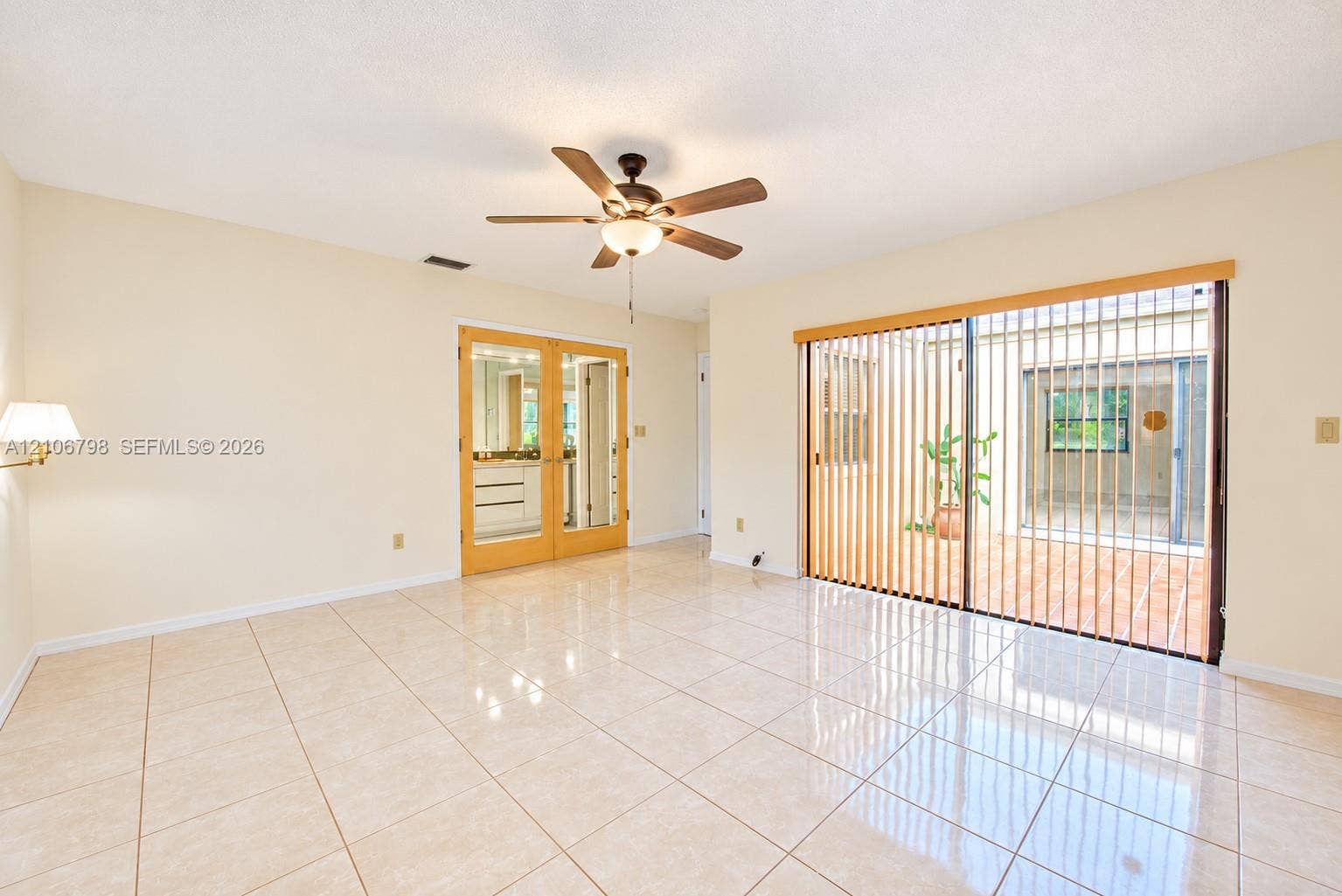 14750 SW 156th Street, Miami, FL 33187 Spacious room featuring polished tile flooring, wood-framed French doors, and large sliding glass doors opening to an enclosed patio area, complemented by a central ceiling fan