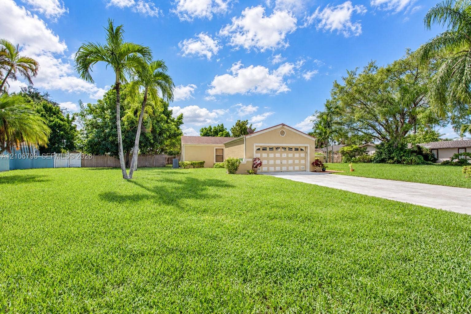 14750 SW 156th Street, Miami, FL 33187 Single-story residence featuring a concrete driveway, multi-panel garage door, manicured lawn, and mature palm trees