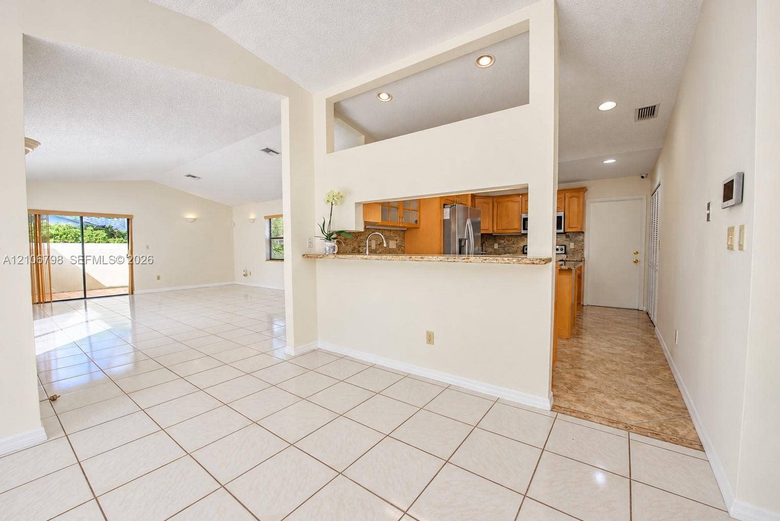 14750 SW 156th Street, Miami, FL 33187 Interior space featuring tile flooring, vaulted ceilings, recessed lighting, a pass-through breakfast bar with stone-surfaced countertop, and natural light via sliding glass doors