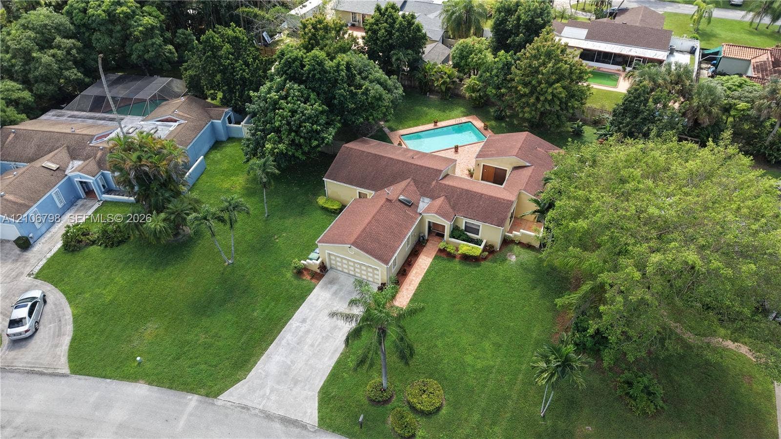 14750 SW 156th Street, Miami, FL 33187 Aerial perspective of a multi-structure property featuring a swimming pool, concrete driveway, expansive lawn, and mature landscaping