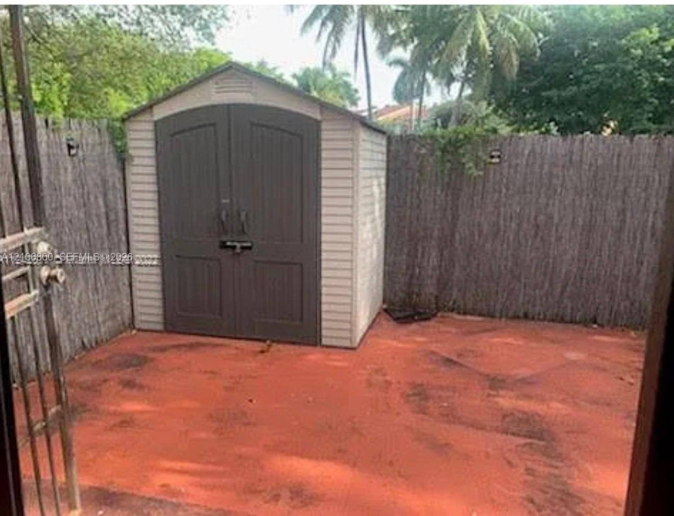 3820 SW 52nd Avenue, Hollywood, Hollywood, FL 33023 Exterior storage shed with double doors, set upon a red-toned concrete patio enclosed by reed fencing and an iron gate