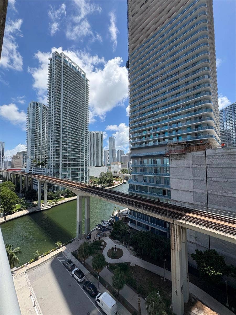 690 SW 1st Court, #1212, Miami, FL 33130 Urban high-rise setting featuring high-density residential towers, an elevated transit rail system, a waterway, and concrete-paved walkways with established palm trees