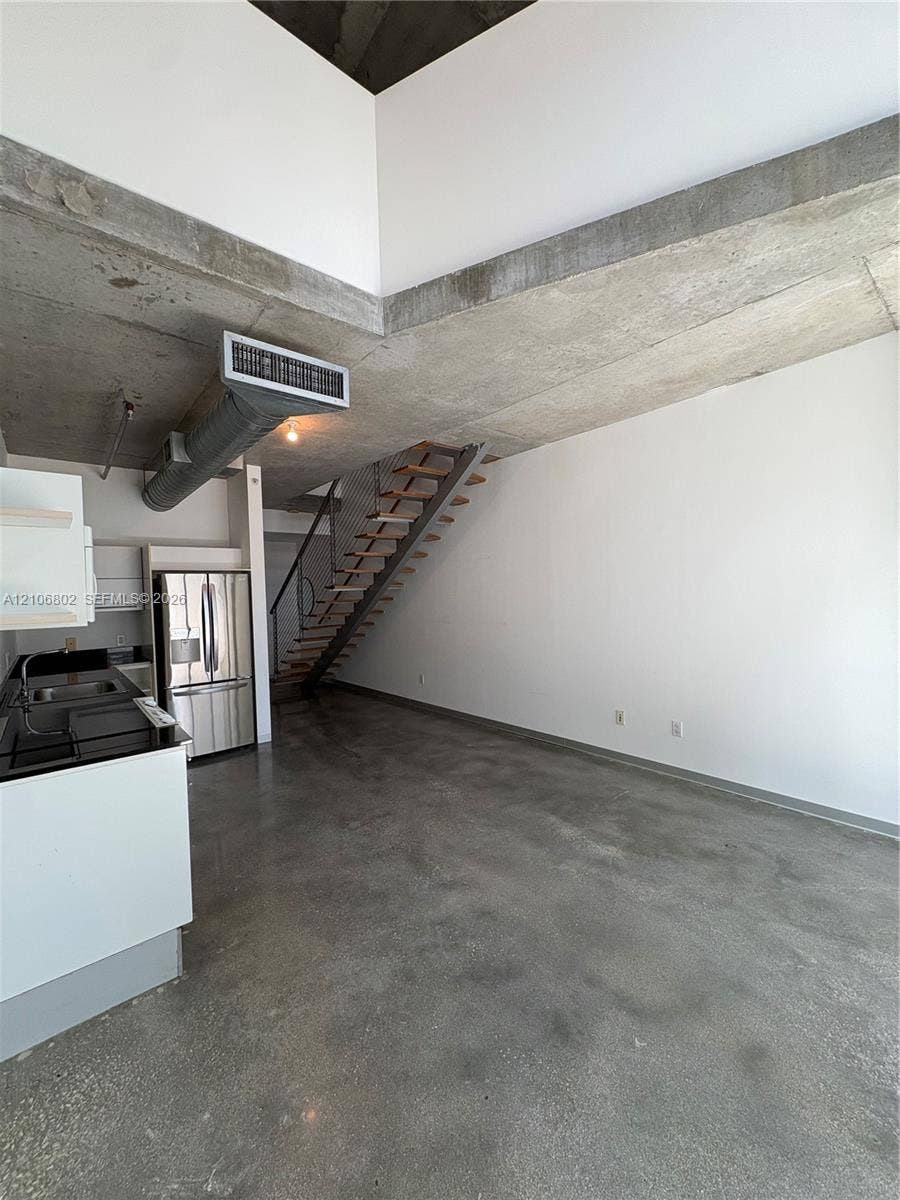 690 SW 1st Court, #1212, Miami, FL 33130 Industrial-style interior featuring high ceilings with exposed concrete beams, polished concrete flooring, a floating staircase with metal railings, and stainless steel kitchen appliances