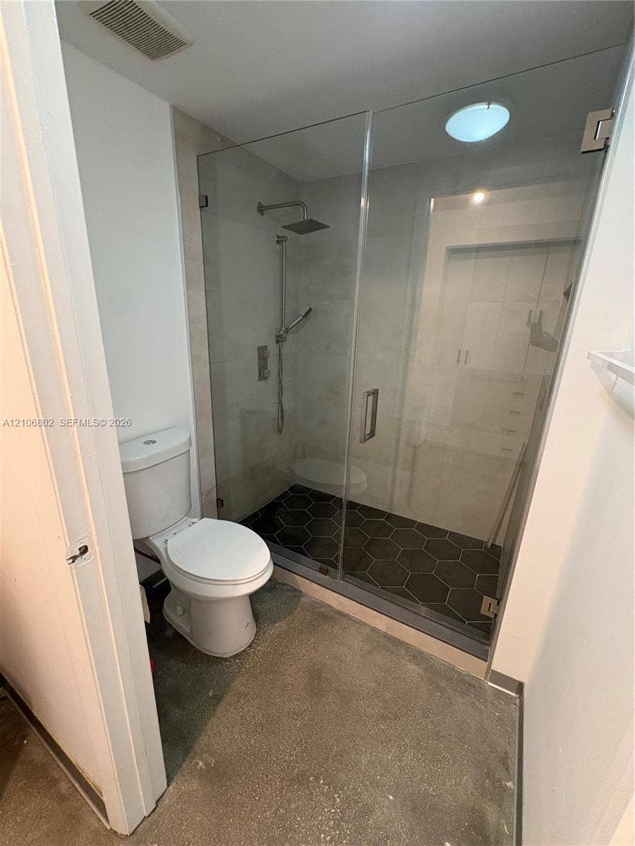 690 SW 1st Court, #1212, Miami, FL 33130 Walk-in shower featuring a frameless glass enclosure, dark hexagonal floor tile, and a rainfall showerhead