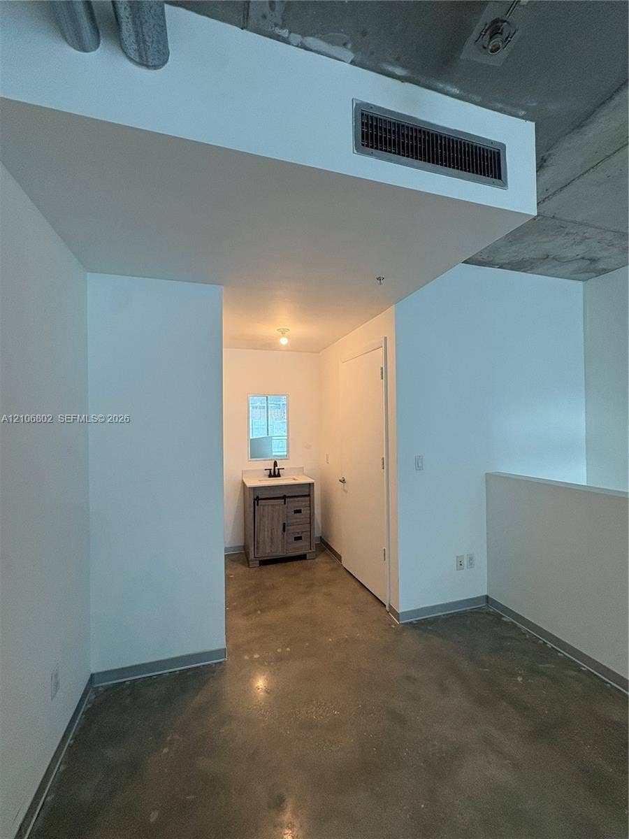 690 SW 1st Court, #1212, Miami, FL 33130 Industrial-style aesthetic featuring exposed concrete ceilings, polished concrete flooring, a vanity with a barn-door style cabinet, a light-toned countertop, and a wall-mounted mirror