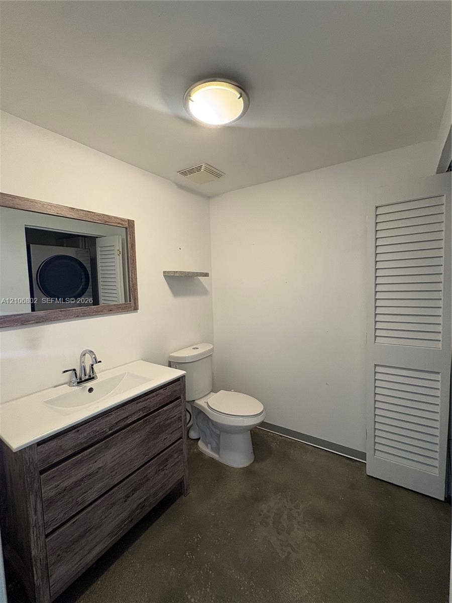 690 SW 1st Court, #1212, Miami, FL 33130 Vanity featuring a dark wood-finish cabinet with a white countertop, integrated sink, and dual-handle faucet, paired with a framed wall mirror, louvered closet doors, and concrete flooring