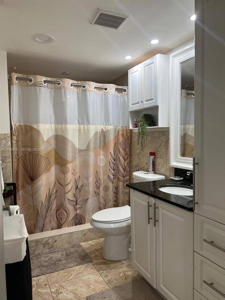 12600 SW 5th Court, #204L, Pembroke Pines, FL 33027 White cabinetry vanity with a dark countertop and integrated sink, stone-finish wall tile, recessed ceiling lighting, and built-in upper storage cabinetry