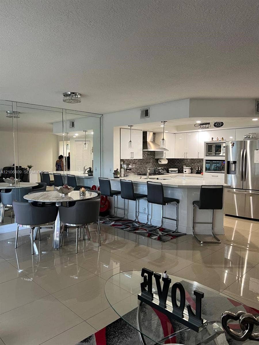 12600 SW 5th Court, #204L, Pembroke Pines, FL 33027 Kitchen featuring high-gloss white cabinetry, quartz countertops, a stone-tile backsplash, and stainless-steel appliances, complemented by polished tile flooring and mirrored wall paneling
