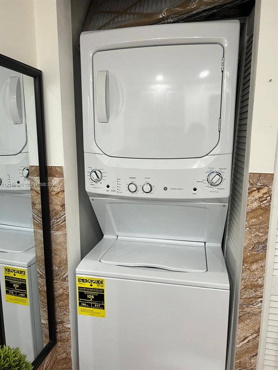 12600 SW 5th Court, #204L, Pembroke Pines, FL 33027 Stacked laundry unit with a white top-loading washer and front-loading dryer, situated within a built-in recessed enclosure featuring decorative stone-finish tile wall accents