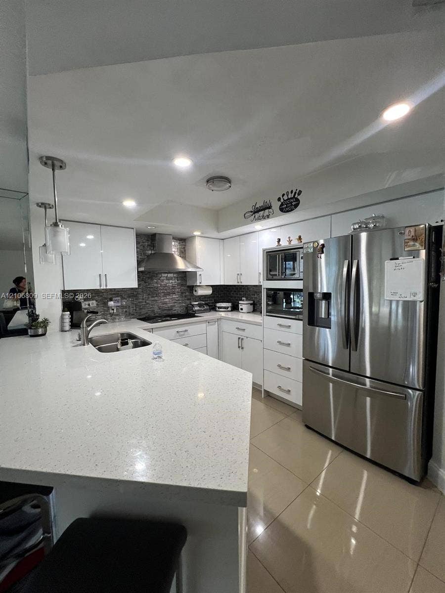 12600 SW 5th Court, #204L, Pembroke Pines, FL 33027 Kitchen featuring a stone-composite countertop, stainless steel appliances, gloss-finish cabinetry, tile flooring, and a glass-tile backsplash