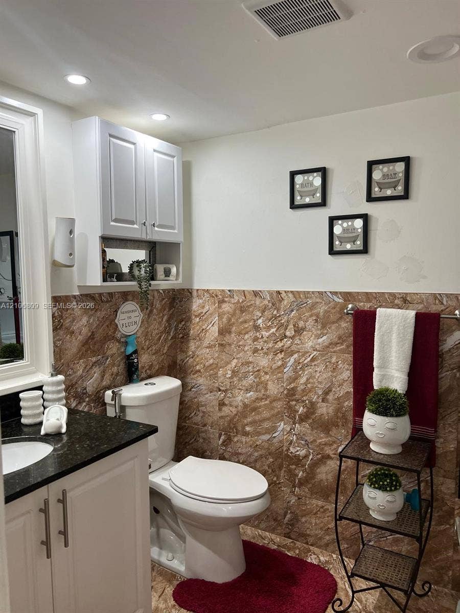12600 SW 5th Court, #204L, Pembroke Pines, FL 33027 Bathroom vanity with a dark countertop and undermount sink, white shaker-style cabinetry, wall-mounted storage cabinet, and stone-finish wall tiling
