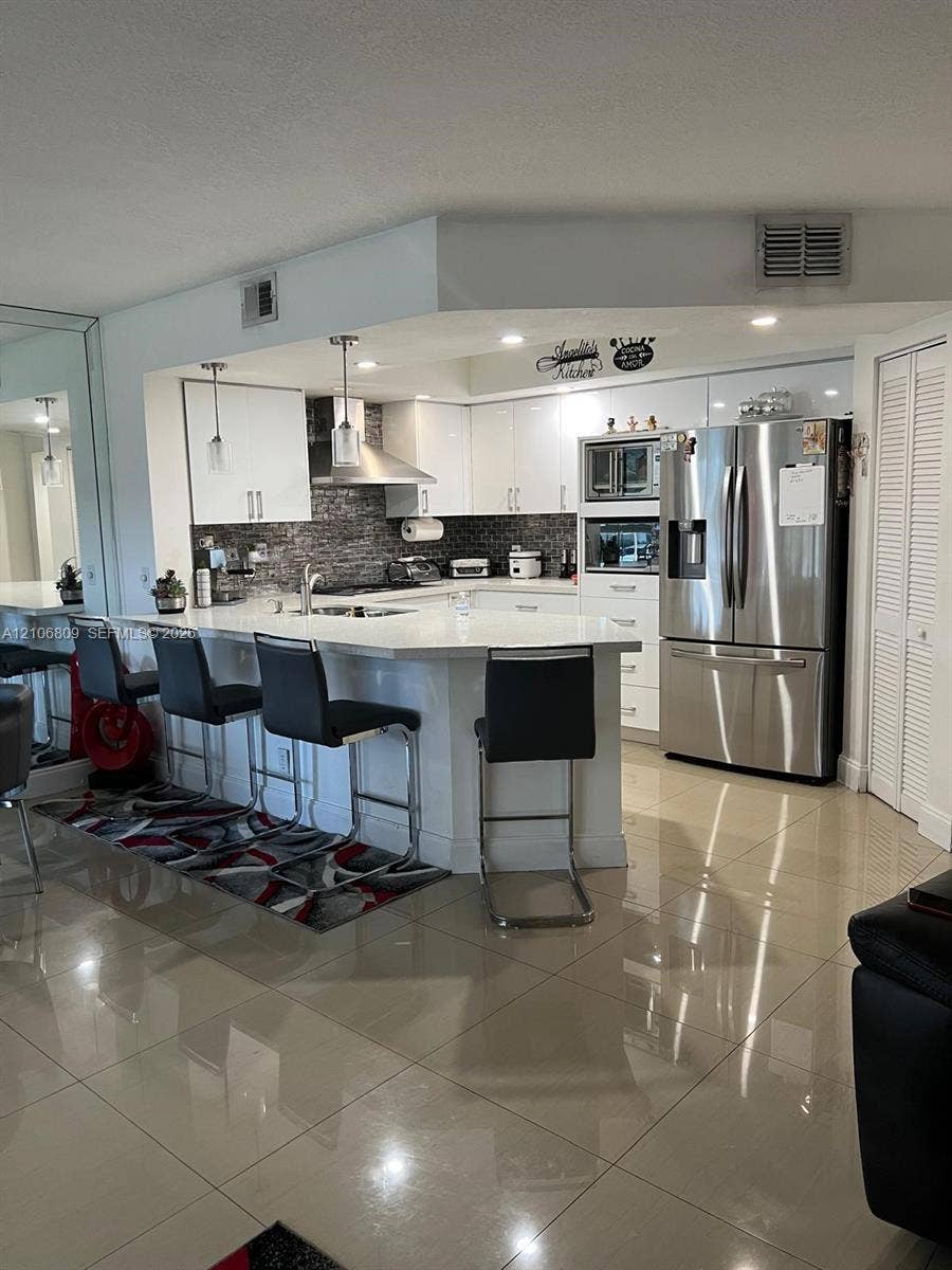 12600 SW 5th Court, #204L, Pembroke Pines, FL 33027 Kitchen featuring white cabinetry, solid-surface countertops, stone-tile backsplash, stainless steel appliances, and large-format tile flooring