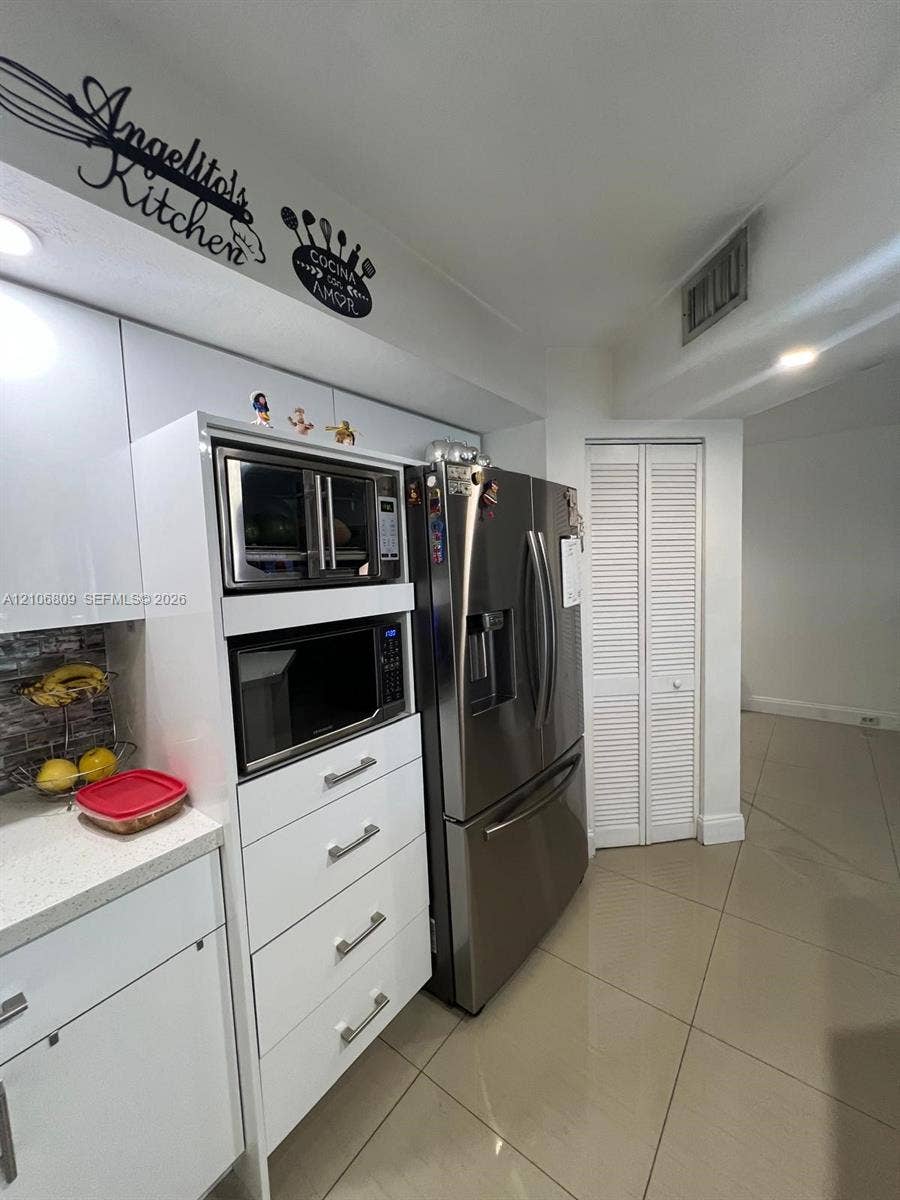 12600 SW 5th Court, #204L, Pembroke Pines, FL 33027 Kitchen featuring high-gloss white cabinetry, stainless steel French-door refrigerator, built-in microwave, stone-finish countertops, and large-format tile flooring