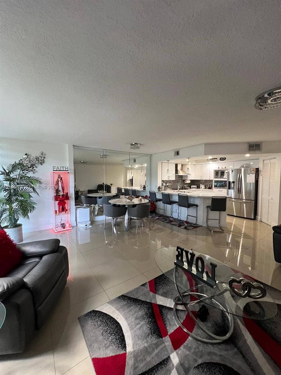 12600 SW 5th Court, #204L, Pembroke Pines, FL 33027 Open-concept living space featuring large-format tile flooring, mirrored wall accents, a kitchen island with stone countertops, stainless steel appliances, and built-in recessed lighting