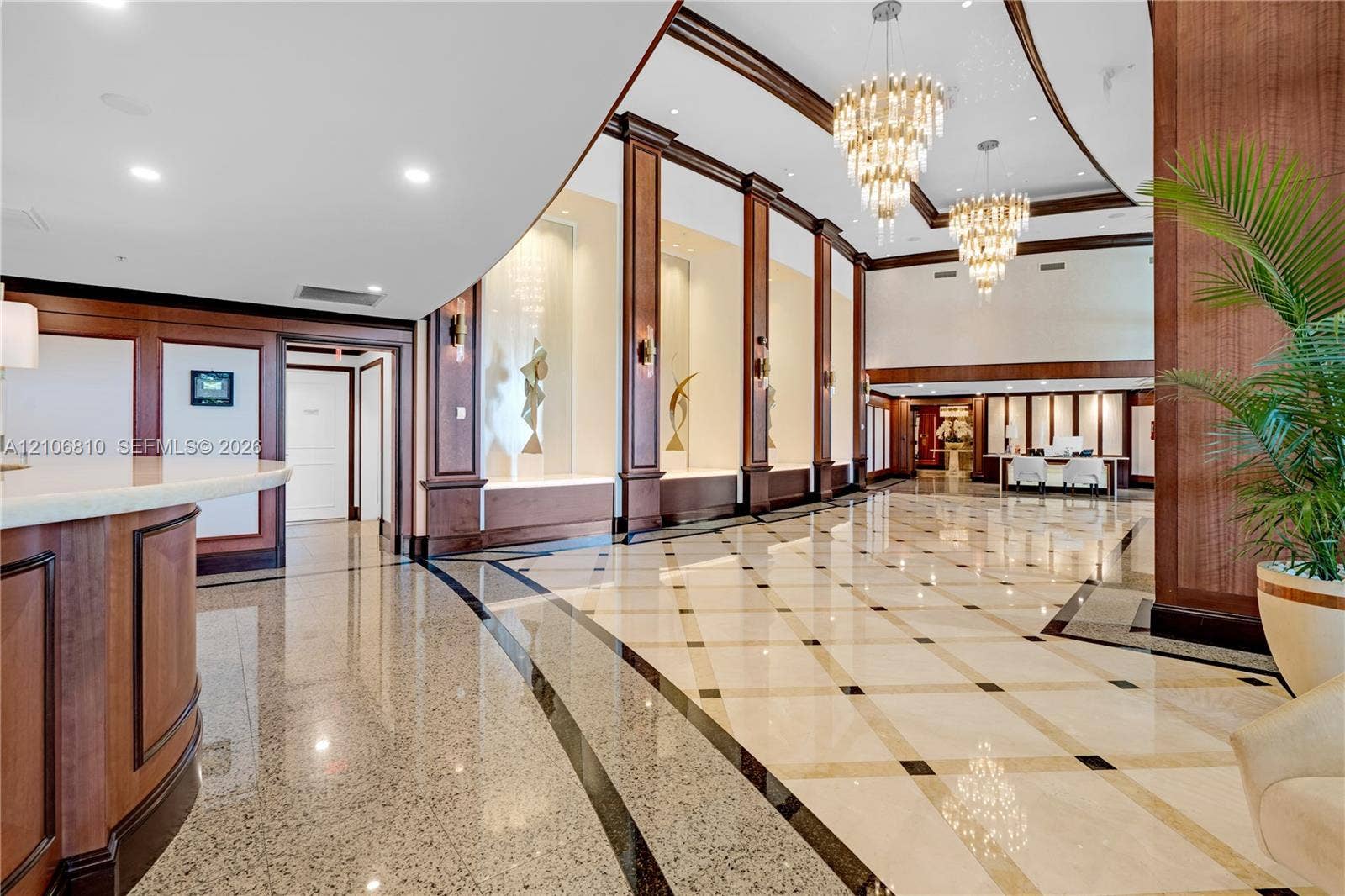 Grand lobby featuring polished stone tile flooring with decorative inlay, extensive wood-paneled columns, tiered crystal chandeliers, and recessed wall display niches