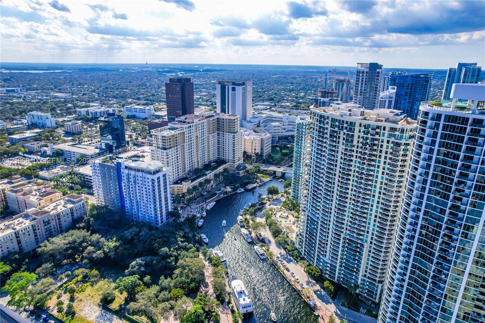 Aerial perspective showcasing a high-density urban environment featuring glass-clad high-rise structures, a central waterway, and surrounding mature canopy