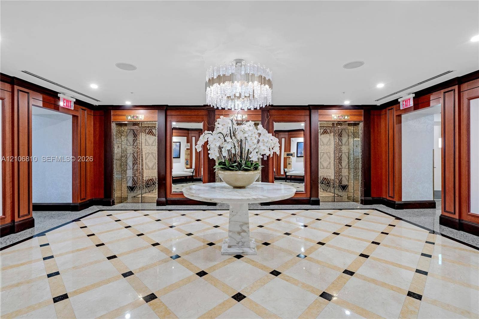 Grand lobby featuring paneled wood walls, geometric stone flooring with inlay accents, integrated elevator banks, and a multi-tiered crystal chandelier