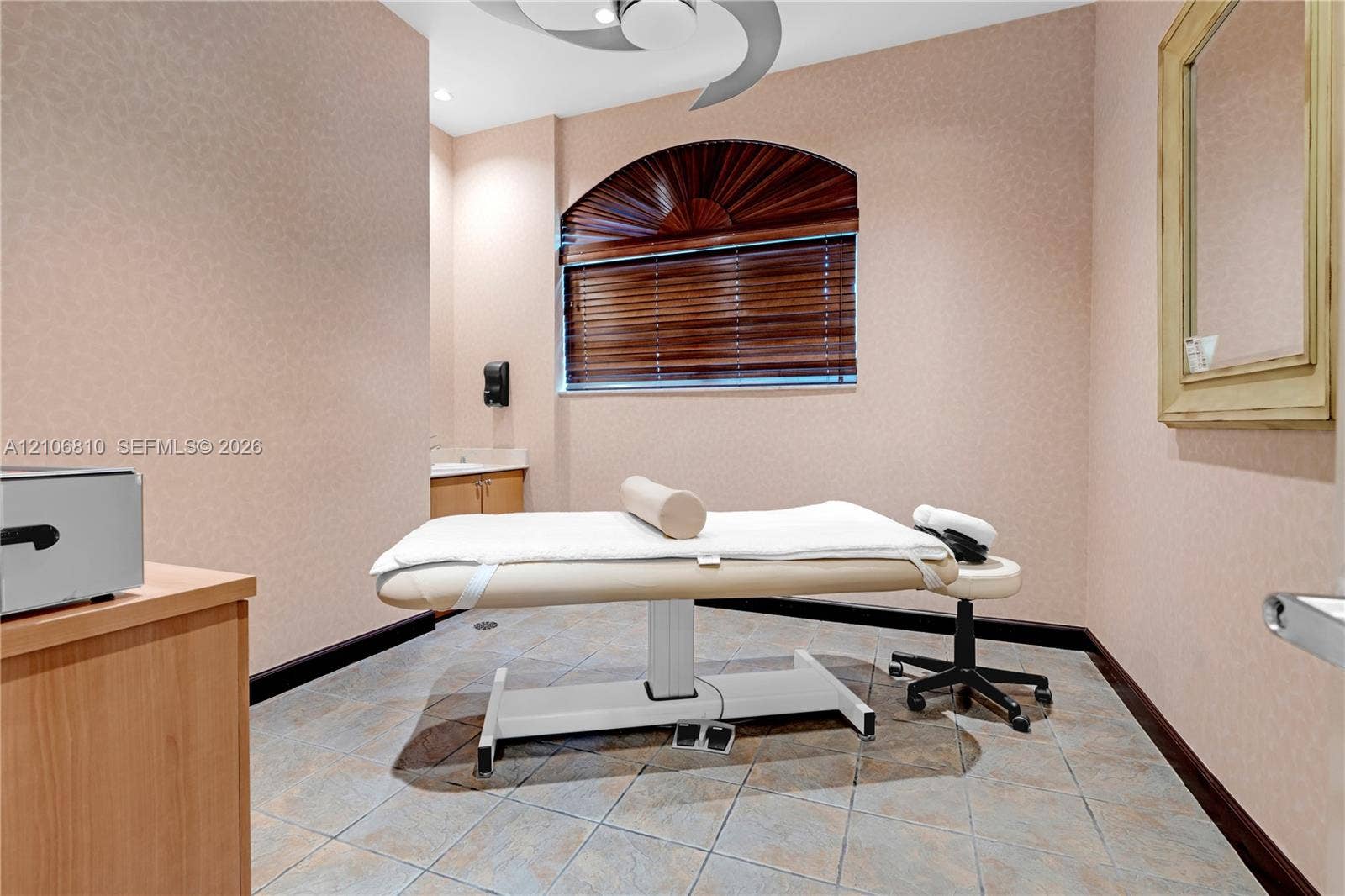 Arched window with wood-finish blinds, neutral wall surfacing, ceiling-mounted fan, tile flooring, and built-in cabinetry with sink