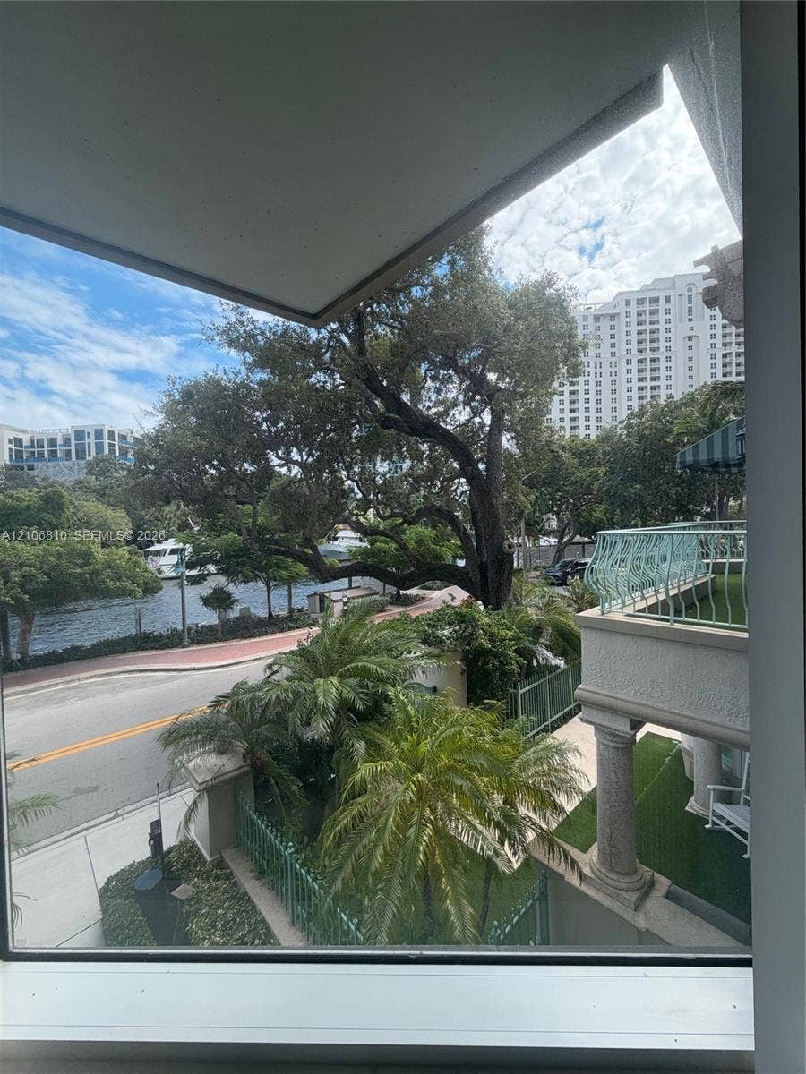 Exterior balcony featuring decorative metal railings, concrete columns, and natural scenery including mature trees, greenery, and water frontage
