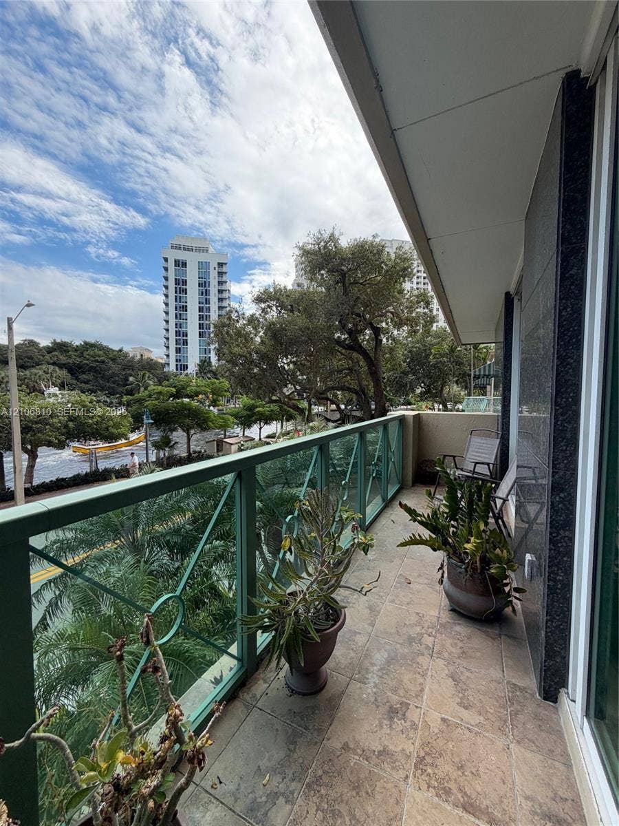 Covered balcony featuring stone-finish tile flooring, decorative metal railing, and high-rise exterior cladding