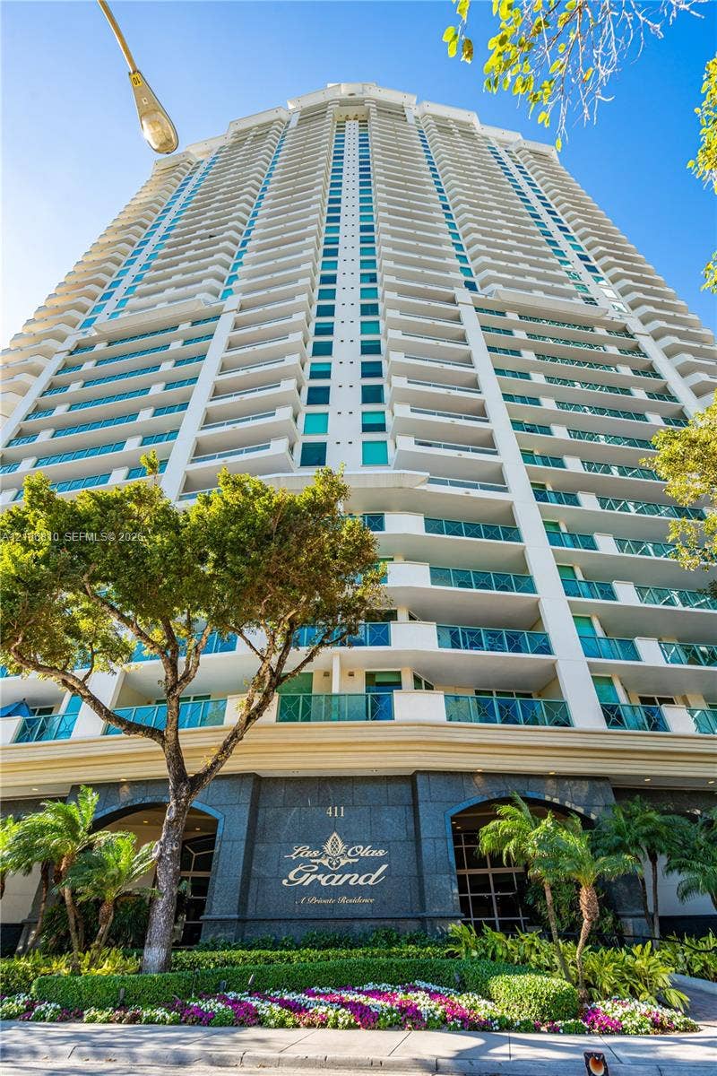 High-rise residential building exterior featuring stacked glass balconies, stone-clad ground level, and manicured landscaping