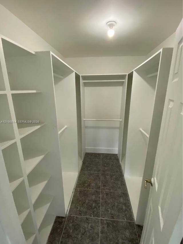 6503 Winfield Boulevard, #211AD, Margate, Margate, FL 33063 Walk-in closet featuring white built-in shelving, multiple hanging rods, and dark tile flooring