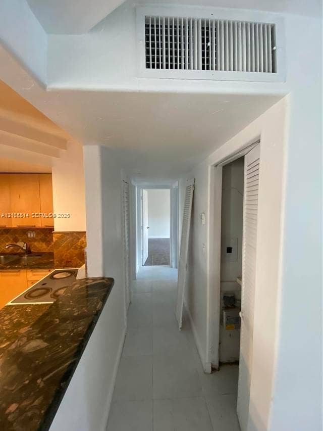 6503 Winfield Boulevard, #211AD, Margate, Margate, FL 33063 Kitchen area featuring natural-finish wood cabinetry, dark stone-surfaced countertops, and white tile flooring
